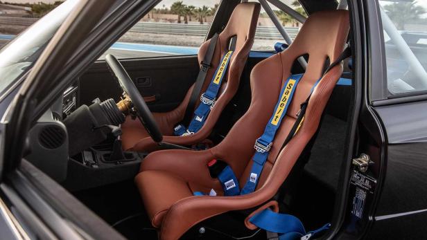 Das Interieur eines Autos mit braunen Ledersitzen und blauen Sabelt-Gurten.