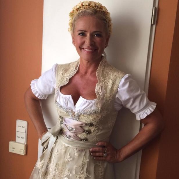 Eine Frau in einem Dirndl mit Blumenkranz lächelt in die Kamera.