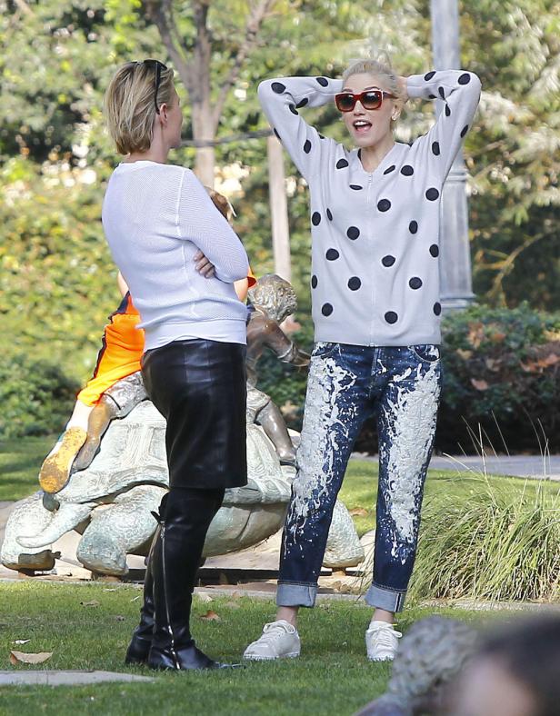 Gwen Stefani mit Sonnenbrille und gepunkteter Jacke unterhält sich im Park mit einer Frau.