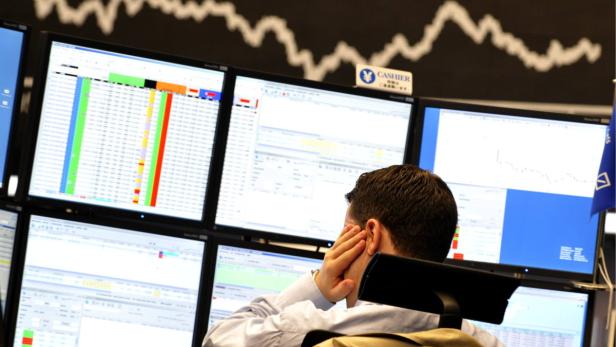 Ein Börsenhändler sitzt vor mehreren Monitoren mit Finanzdaten.