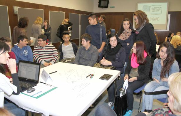 Eine Gruppe junger Leute sitzt an einem Tisch und diskutiert über digitale Medien.