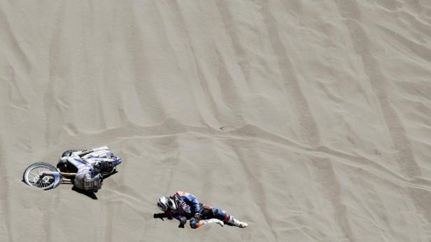 Ein Motocross-Fahrer liegt neben seinem gestürzten Motorrad im Sand.