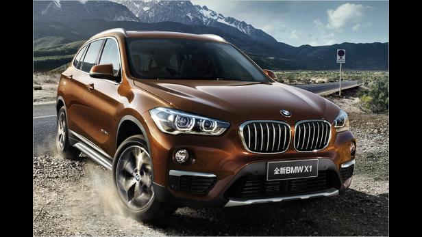 Ein brauner BMW X1 fährt auf einer Schotterstraße vor einer Bergkulisse.