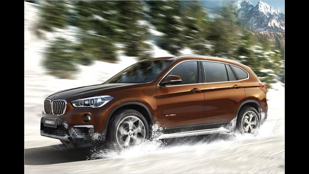 Ein brauner BMW X1 fährt durch eine verschneite Landschaft.