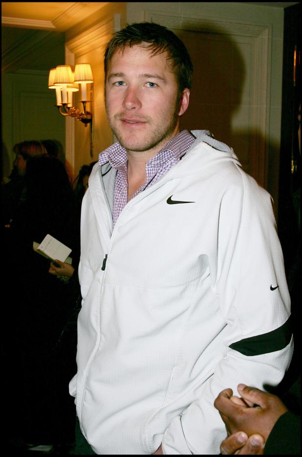 Ein Mann mit kurzer brauner Haaren und einer weißen Nike-Jacke steht in einem Raum.