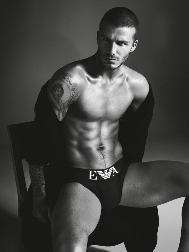 Schwarz-Weiß-Porträt von David Beckham, der auf einem Stuhl sitzt und Unterwäsche von Emporio Armani trägt.