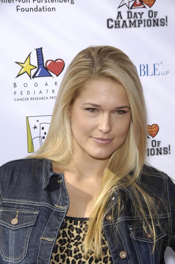 Eine Frau mit blonder Haare und Jeansjacke vor einem Sponsorenhintergrund.