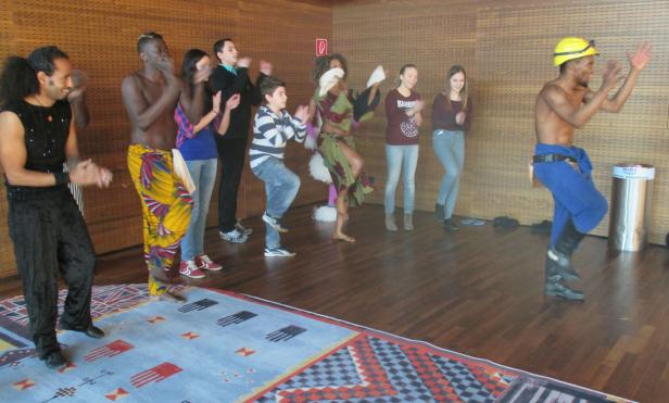 Eine Gruppe von Menschen tanzt und klatscht in einem Raum mit Holzboden.