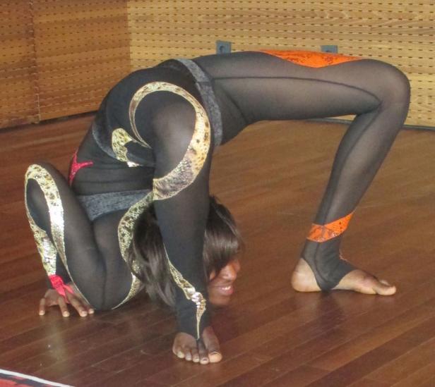 Eine Frau in einem schwarzen, schlangenverzierten Anzug führt eine extreme Yoga-Pose aus.