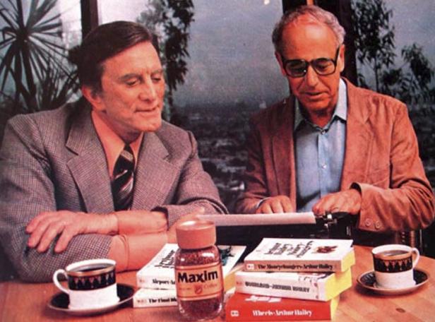 Kirk Douglas und Arthur Hailey an einem Tisch mit Büchern, Kaffee und einer Maxim-Kaffeedose.