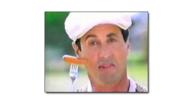Sylvester Stallone mit einem Hotdog auf einer Gabel vor seinem Gesicht.