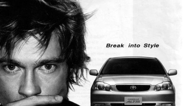 Schwarzweißaufnahme von Brad Pitt neben einem Toyota Corolla Altis.