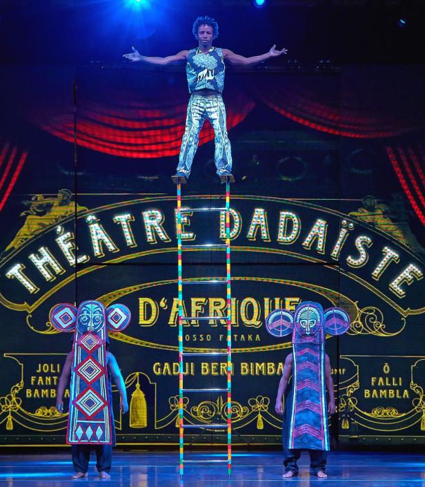 Ein Akrobat balanciert auf einer Leiter vor der Bühnenshow „Théâtre Dadaiste D'Afrique“.