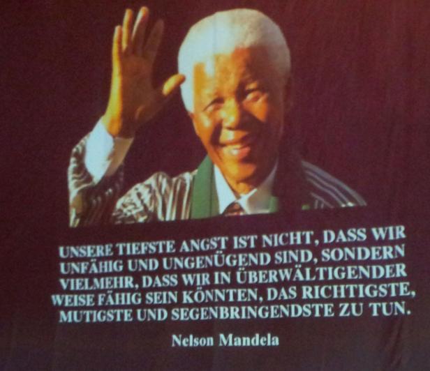 Ein Porträt von Nelson Mandela, der lächelt und die Hand zum Gruß hebt.