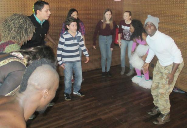 Eine Gruppe von Menschen steht in einem Raum mit Holzboden und scheint sich zu amüsieren.
