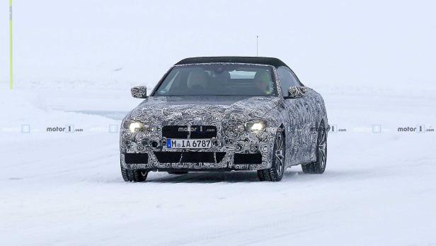 Ein getarntes BMW 2er Cabriolet fährt auf einer schneebedeckten Straße.