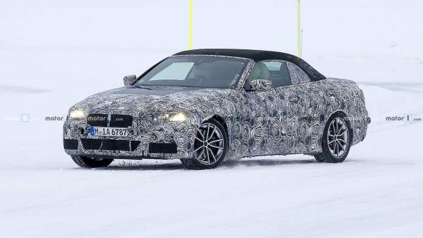 Ein getarntes BMW 2er Cabrio fährt auf einer schneebedeckten Straße.