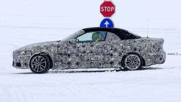 Ein getarntes Cabriolet fährt auf einer schneebedeckten Straße an einem Stoppschild vorbei.