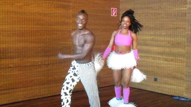 Ein Mann und eine Frau in Kostümen tanzen vor einer Holzwand.