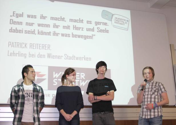 Vier junge Leute stehen vor einer Leinwand mit dem Zitat „Egal was ihr macht, macht es gerne.“.