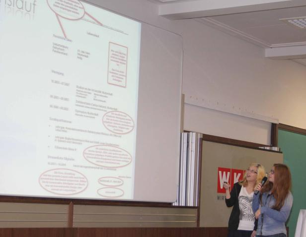 Zwei Frauen präsentieren einen Lebenslauf auf einer Leinwand.