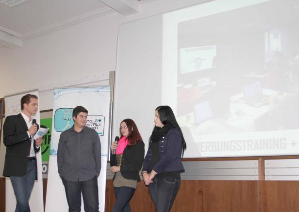 Vier Personen stehen auf einer Bühne während einer Präsentation.