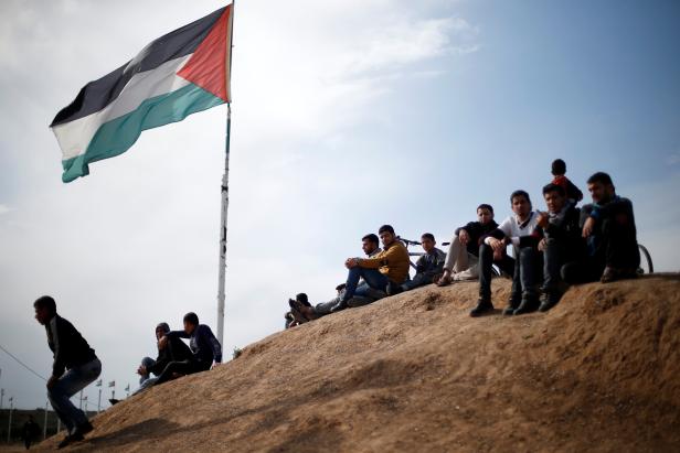 Palestinian sit near to the Israeli-Gaza border fence, ahead of the first anniversary of border protests, east of Gaza City