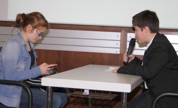 Ein Mädchen tippt auf ihrem Handy, während ein Junge ein Mikrofon hält.