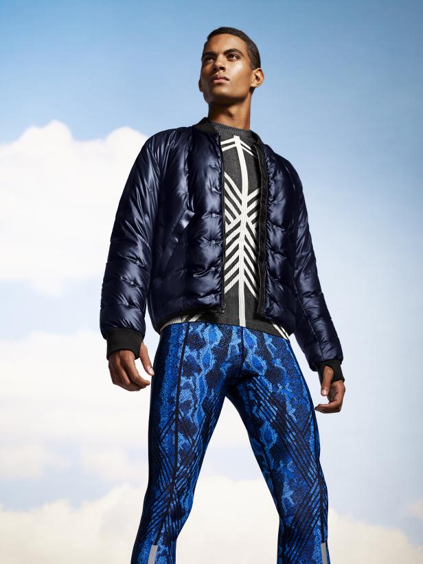 Ein Mann mit blauen Leggings und Daunenjacke steht vor einem Himmel mit Wolken.