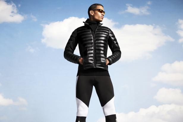 Ein Mann mit Sonnenbrille, schwarzer Jacke und Leggings vor einem Himmel mit Wolken.