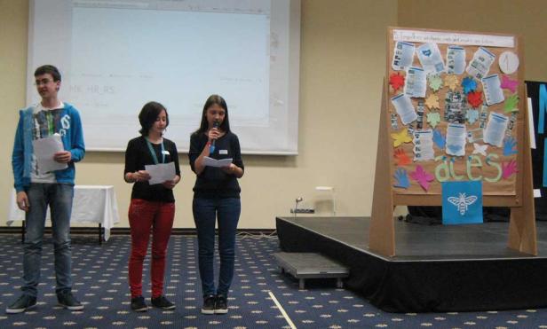 Drei Jugendliche präsentieren auf einer Bühne ein Projekt mit dem Titel „aces“.