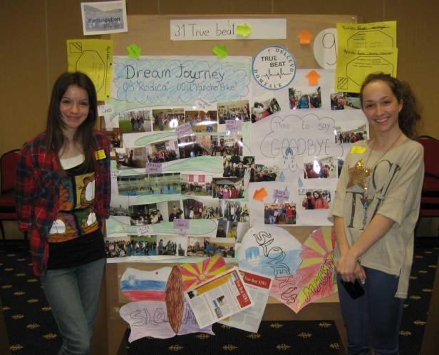 Zwei junge Frauen stehen vor einer Pinnwand mit dem Titel „Dream Journey“ und Fotos von Schüleraustauschaktivitäten.