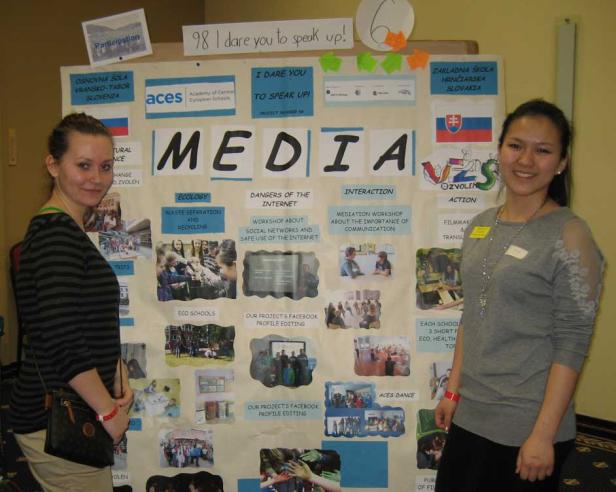 Zwei Frauen stehen vor einer Tafel mit dem Titel „Media“ und Informationen zu Schulprojekten.