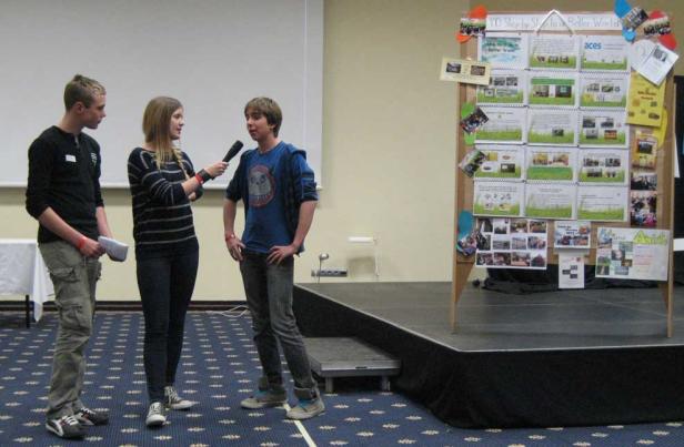 Eine junge Frau interviewt einen Jungen mit einem Mikrofon auf einer Bühne.