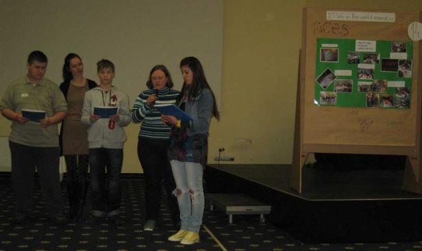 Eine Gruppe von Menschen steht auf einer Bühne vor einer Präsentationstafel.