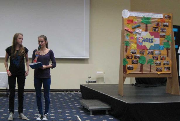 Zwei junge Frauen präsentieren ein Projekt mit dem Titel „Faces“ auf einer Bühne.