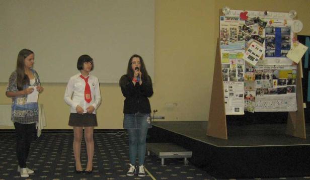 Drei junge Frauen stehen auf einer Bühne vor einem Poster.