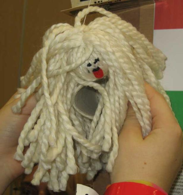 Eine handgemachte Puppe mit weißem Wollhaar wird von Händen gehalten.