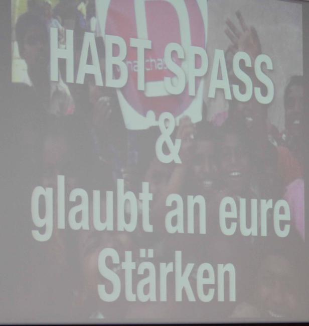 Eine Gruppe von Menschen steht hinter einem Schild mit der Aufschrift „Habt Spaß & glaubt an eure Stärken“.