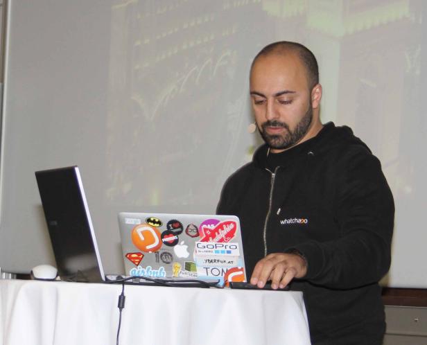 Ein Mann mit Bart steht an einem Tisch mit Laptops und Stickern.