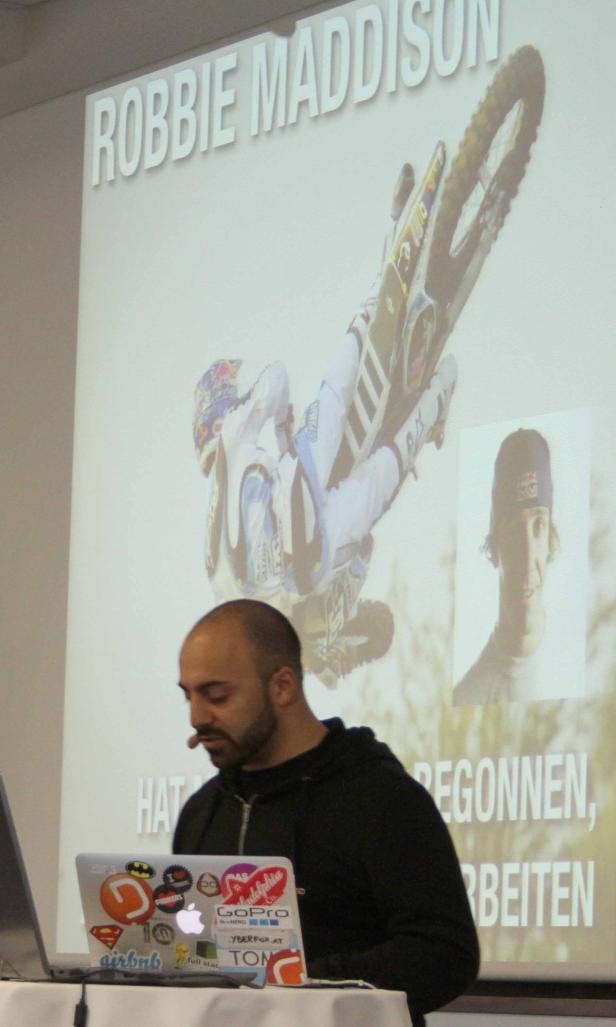 Ein Mann mit Mikrofon hält eine Präsentation über Robbie Maddison.