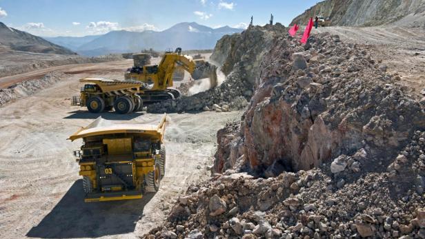 Ein gelber Bagger und Muldenkipper arbeiten in einem Tagebau in den Bergen.