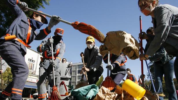Eine Gruppe von Menschen in Arbeitskleidung reinigt eine Straße mit Besen und Müllsäcken.