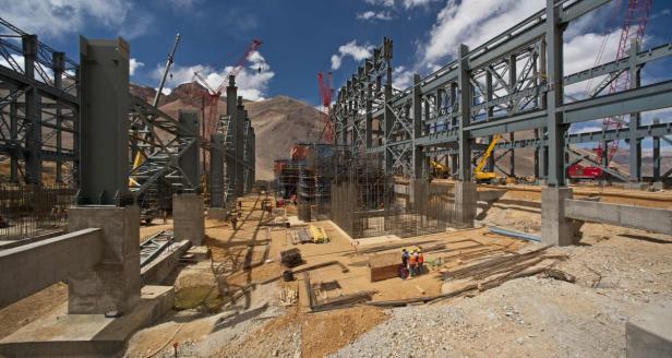 Eine Baustelle mit Stahlkonstruktionen und Kränen vor einer Bergkulisse.