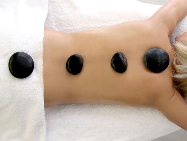 Eine Frau liegt auf einer Liege mit heißen Steinen auf ihrem Rücken.