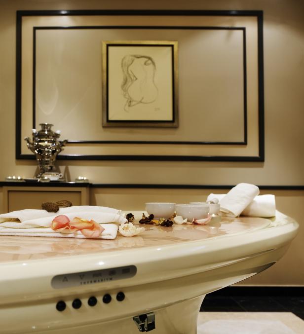 Ein Massagetisch mit Handtüchern, Rosenblättern und Schalen in einem Spa.