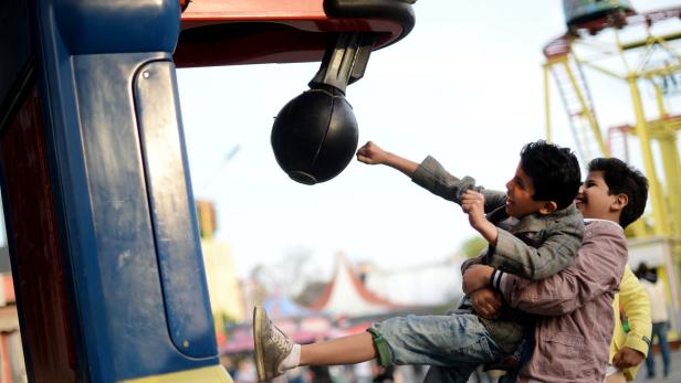 Zwei Jungen schlagen auf einem Jahrmarkt gegen einen Boxball.