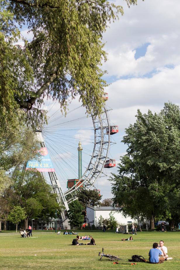 Das Wiener Riesenrad im Prater mit Menschen auf einer Wiese im Vordergrund.