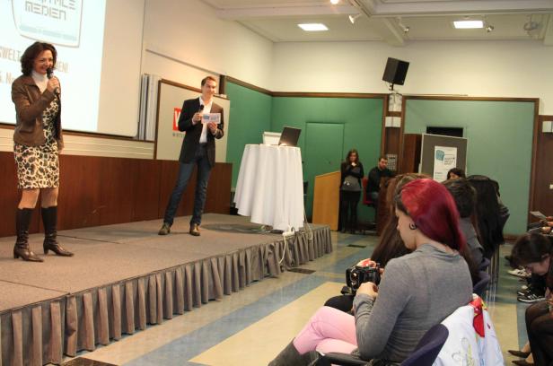 Eine Frau spricht auf einer Bühne in ein Mikrofon, während ein Mann daneben steht und etwas vorliest.