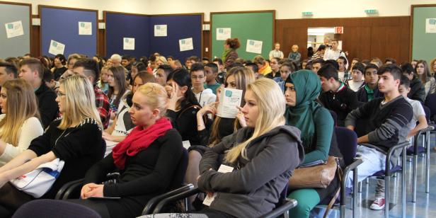 Viele junge Menschen sitzen in einem Raum und hören aufmerksam zu.